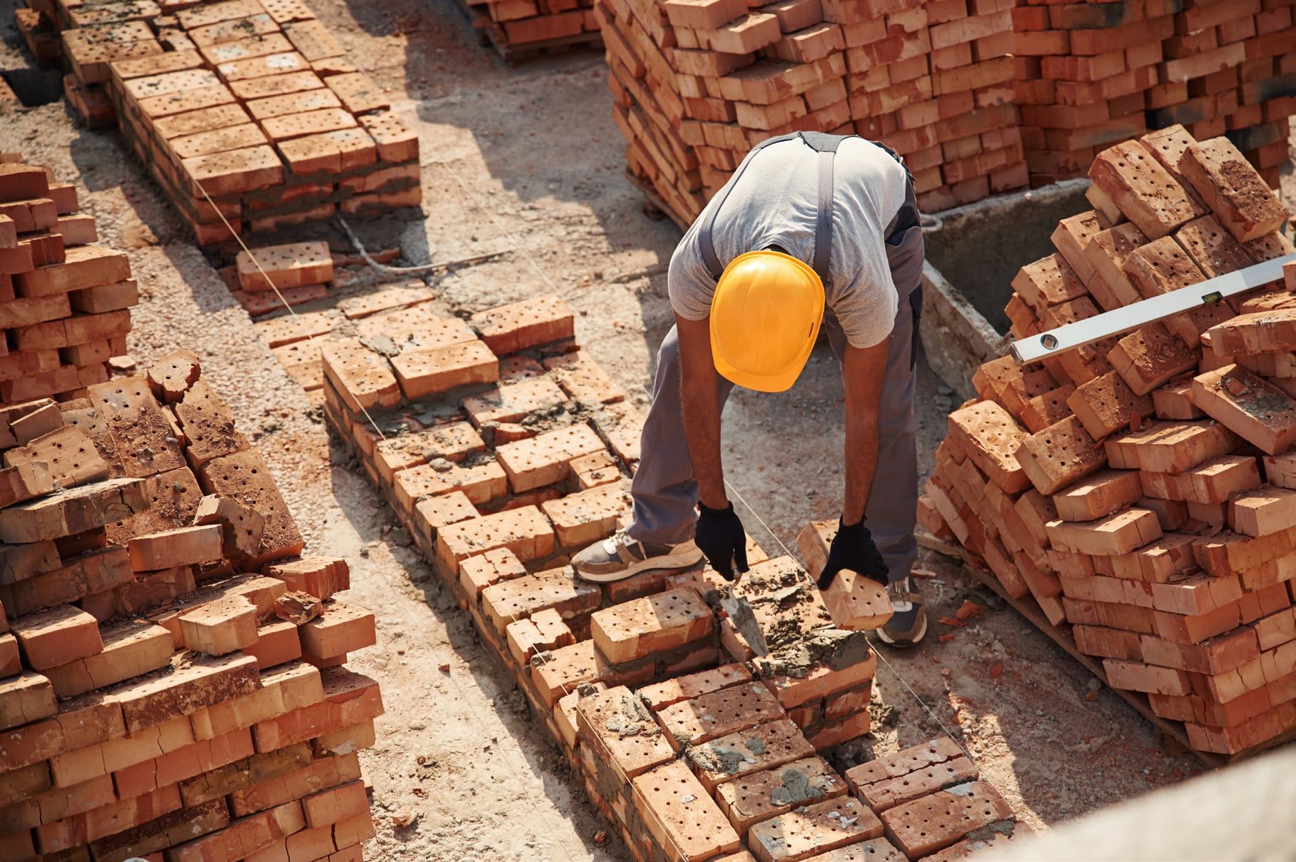 Worker in a hard hat laying paving bricks on a site stacked with clay bricks