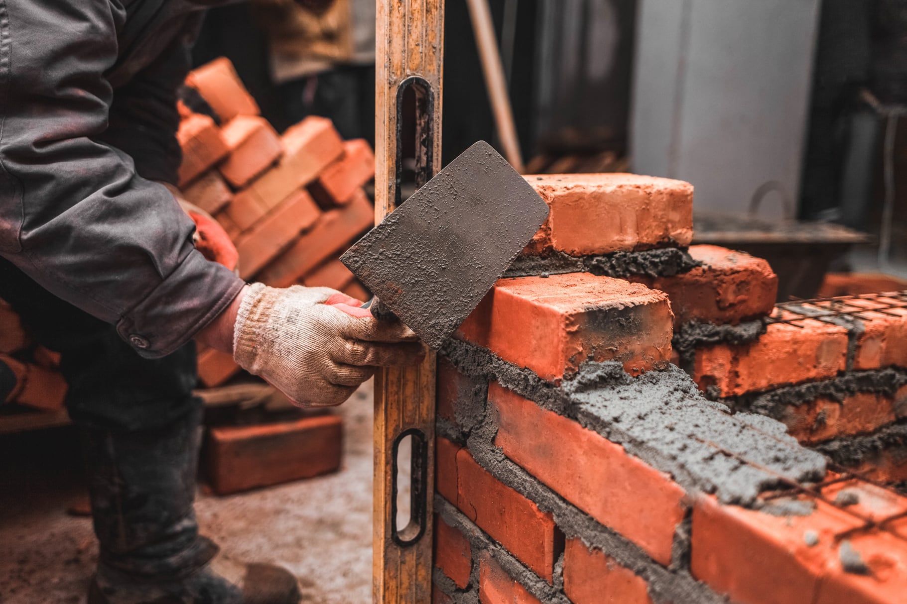 Bricklayer spreading mortar along a course of clay bricks